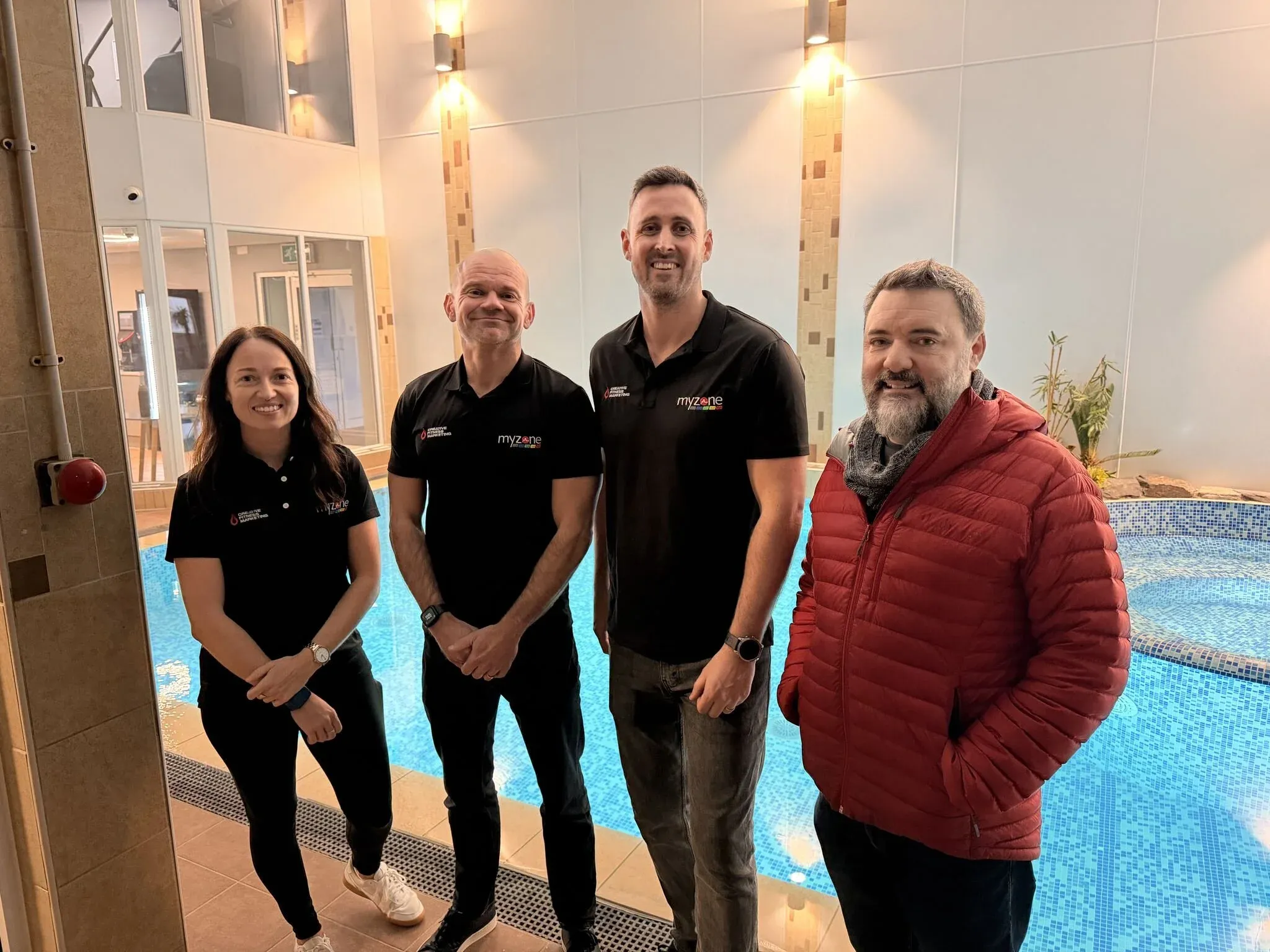 A team of five in matching black polo shirts with Chris, standing beside an indoor pool